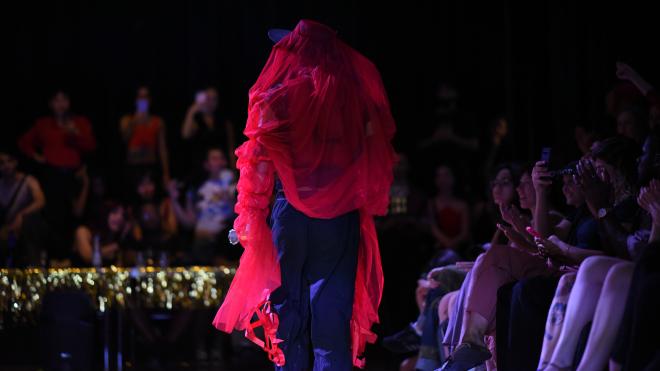 A person in flamboyant red clothing is walking down the cat walk at the ballroom session.