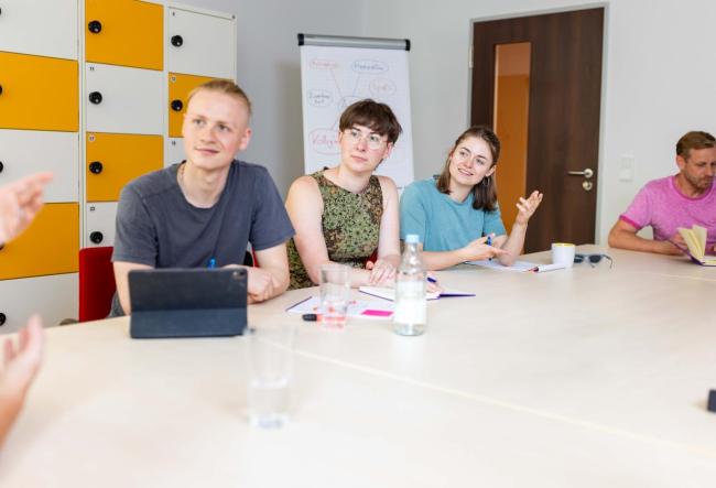 Students in the seminar room with various work utensils on the table, discussing with the lecturer.