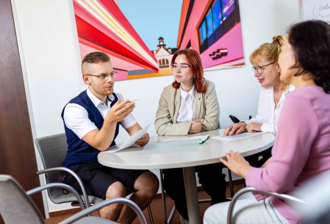 Colleagues at a round table in a meeting where discussions take place.