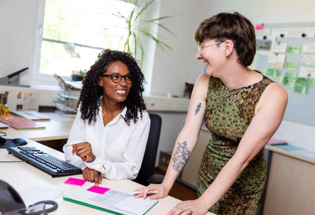 Two colleagues exchange ideas at their office workstation.