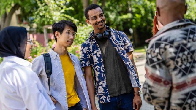 Group of students of international origin stand together and talk animatedly.