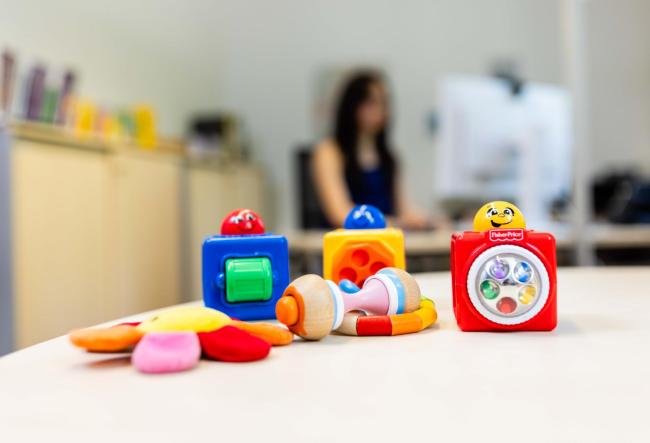 Children's toys on a desk. In the background you can see a mother sitting at her PC.