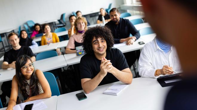 Students in a seminar room, many of them smile and answer their questions.