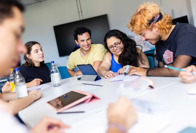 Students in a seminar room working together on something and helping each other.