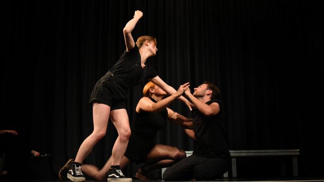 Three actors are playing in improv scene. One appears to be stabbing the other.