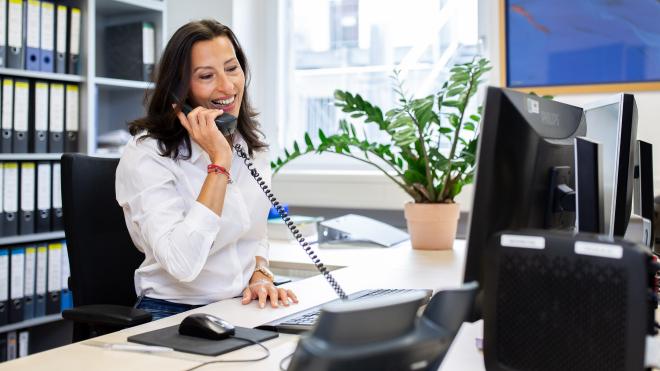 Clerk at her desk with phone in hand, smiling in a friendly manner.