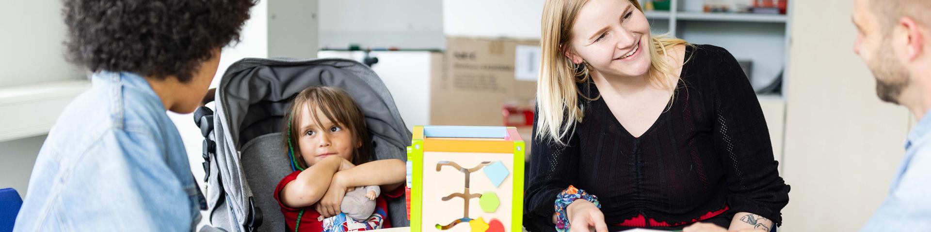 Students with small children seek advice at a counselling centre. Everyone smiles nicely at each other.