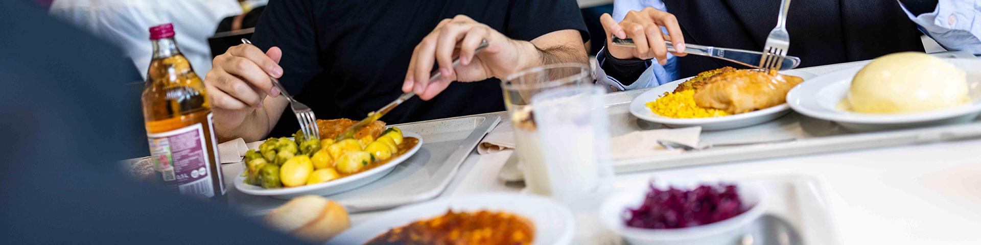 Students eat their Mensa meal, consisting of several components and drinks. The food is placed on the cafeteria trays.