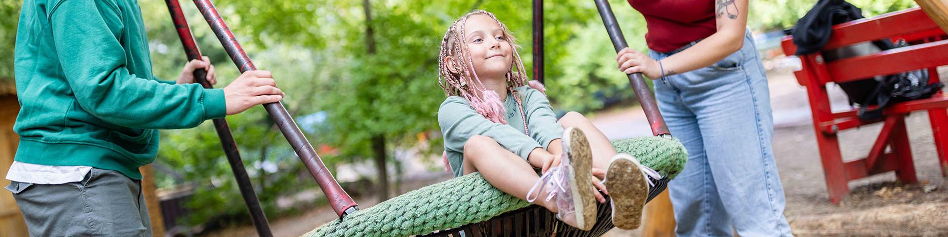 A toddler is being rocked by two people on a playground and is happy about it.