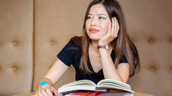 A woman supports her head with her hand and sits at a table with books