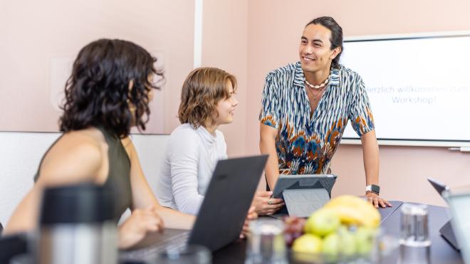 Man leaning on a table and talking to two other people 