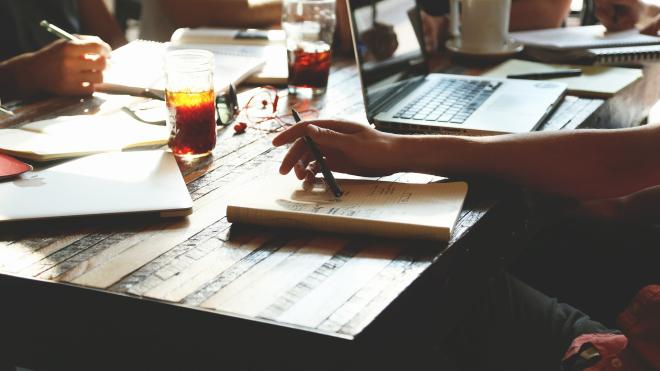 People sitting at a wooden table with open books and drinks