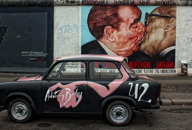 Mauerstück der Berliner Mauer zeigt den ikonischen „Bruderkuss“ zwischen Breschnew und Honecker, mit einem Trabant davor