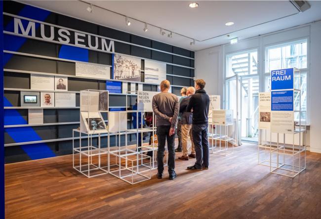 two person are standing in the front of a wall, there is written museum