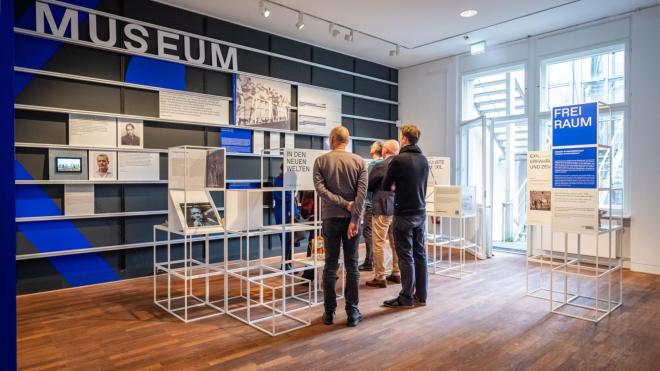 two person are standing in the front of a wall, there is written museum