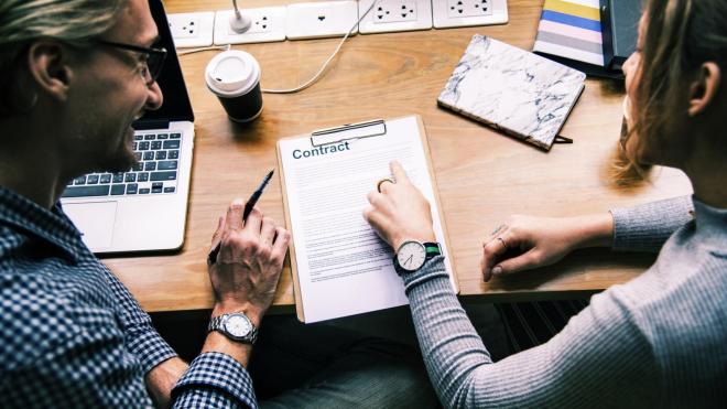 Two people sitting at a table and reading contract papers together.