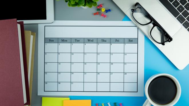 Table with books, a cup of coffee, a laptop, a pair of glasses and a time table in the middle of it