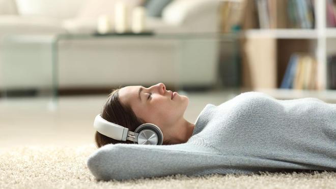 A woman lying on the carpet floor with her headphones on