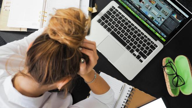 A woman sits in front of a laptop with her head bowed.