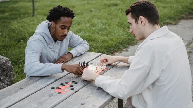 Zwei Personen spielen konzentriert Schach auf einer Bank im Park.